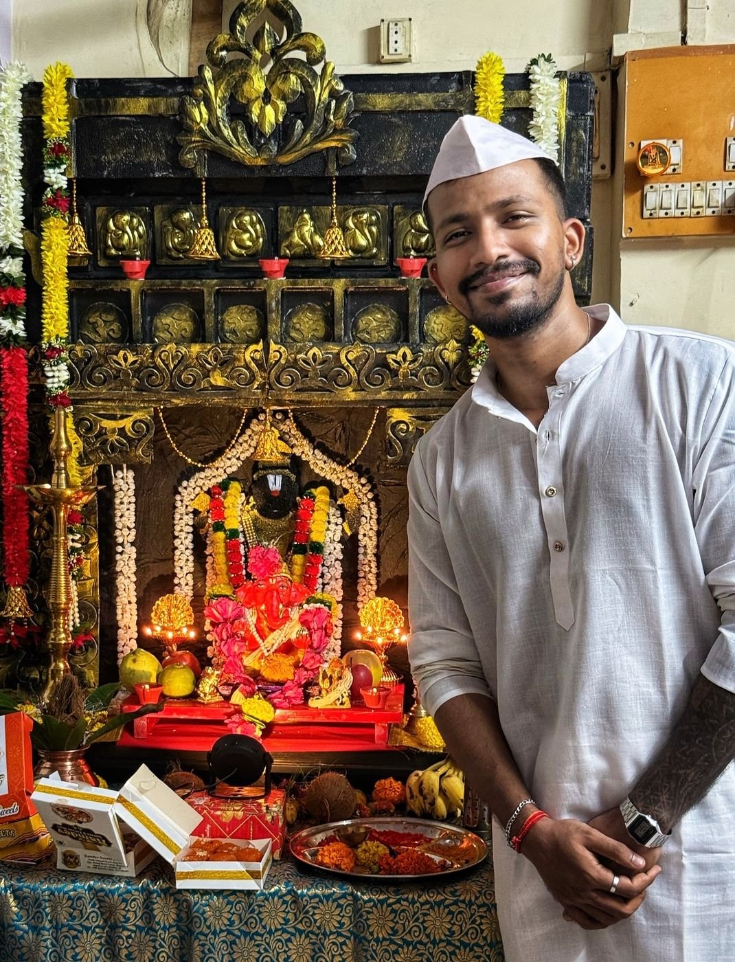 Ninad in a white kurta and cap beside his home Ganpati