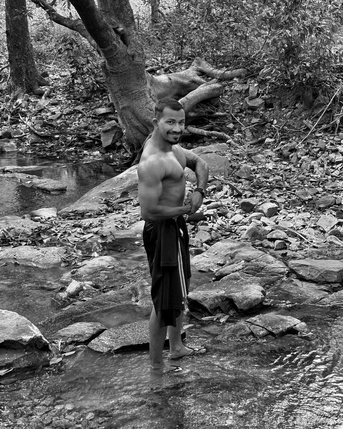 Black and white photo of Ninad flexing by a stream